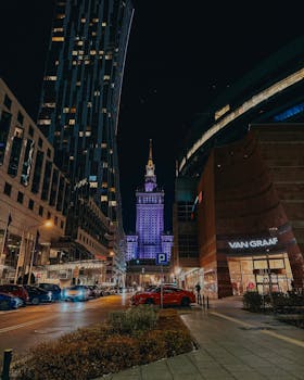 Stunning night view of the Palace of Culture and Science in Warsaw with modern architecture in the foreground.