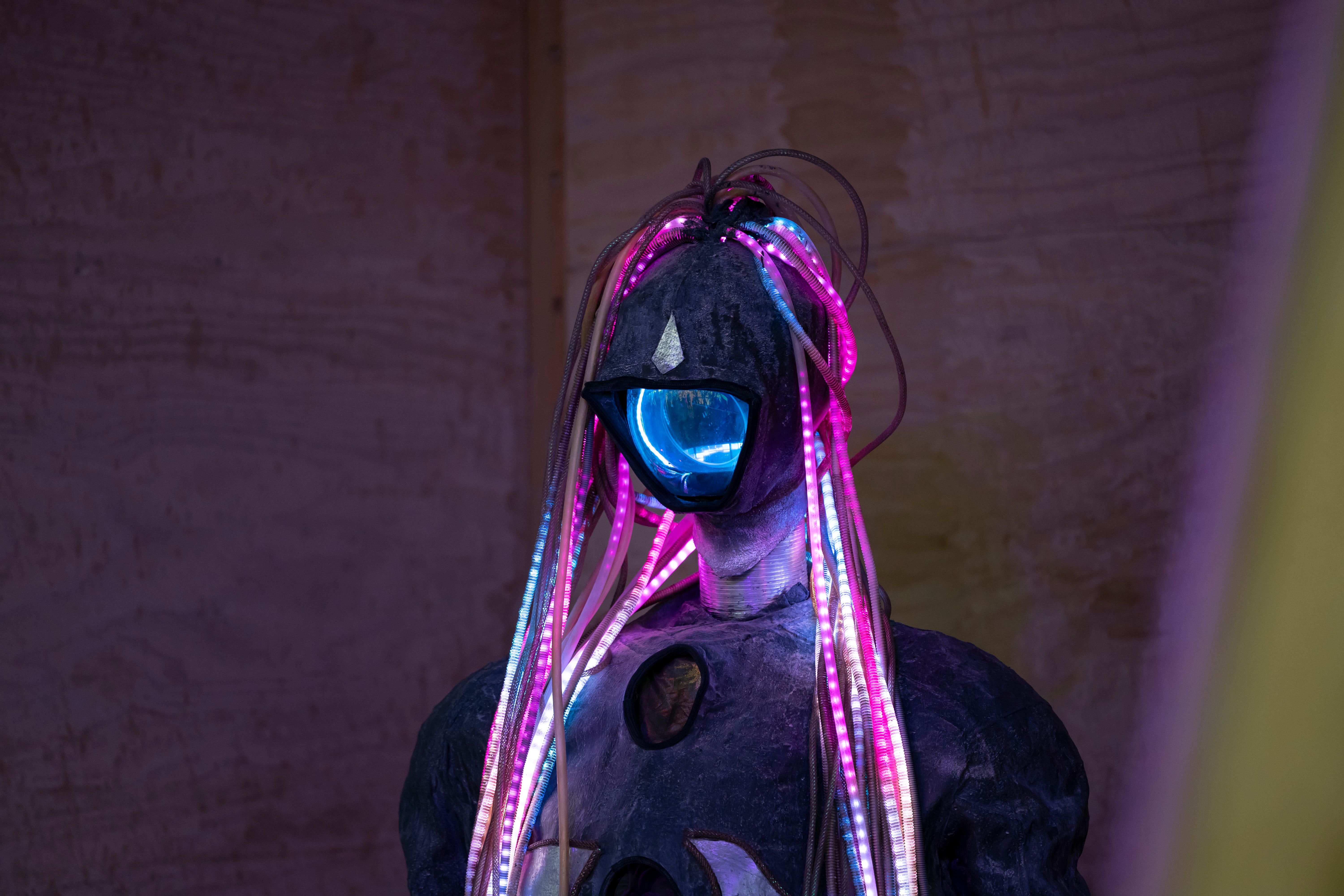 A futuristic humanoid figure adorned with colorful LED lights in a dimly lit environment.