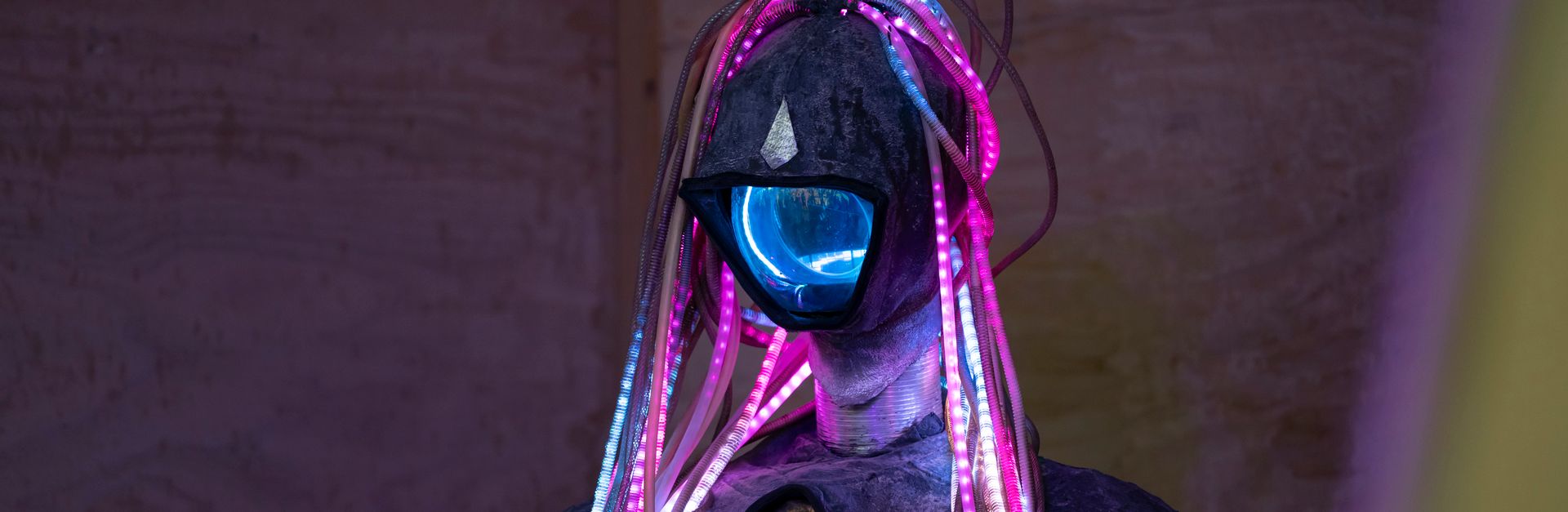 A futuristic humanoid figure adorned with colorful LED lights in a dimly lit environment.