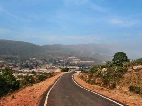 Picturesque rural road winding through lush hills under a clear blue sky.