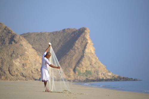 Free A fisherman casts his net on the serene As Sifah beach by the rocky Omani coastline. Stock Photo