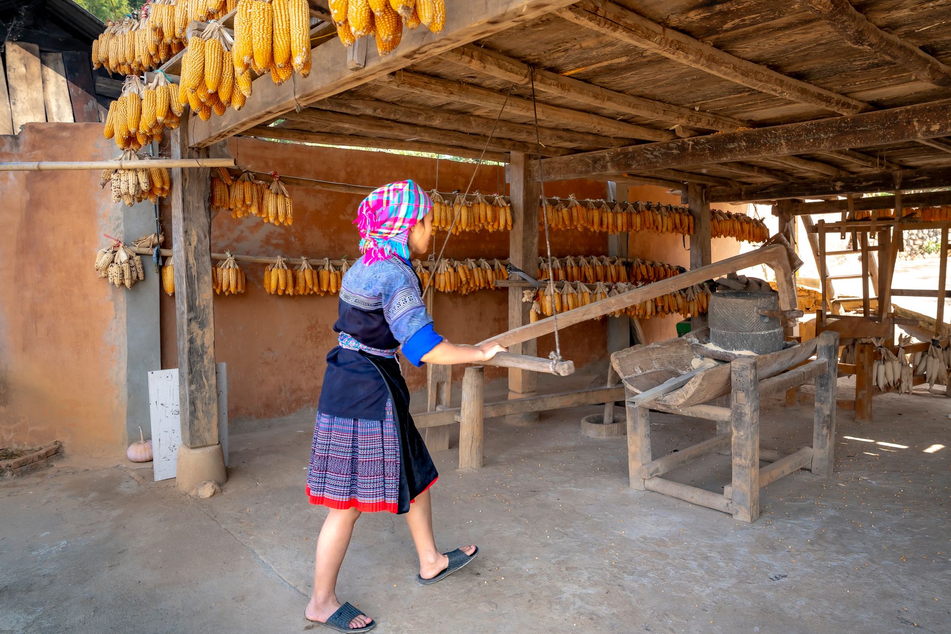 Woman in traditional attire grinding corn in a rural Vietnamese setting.