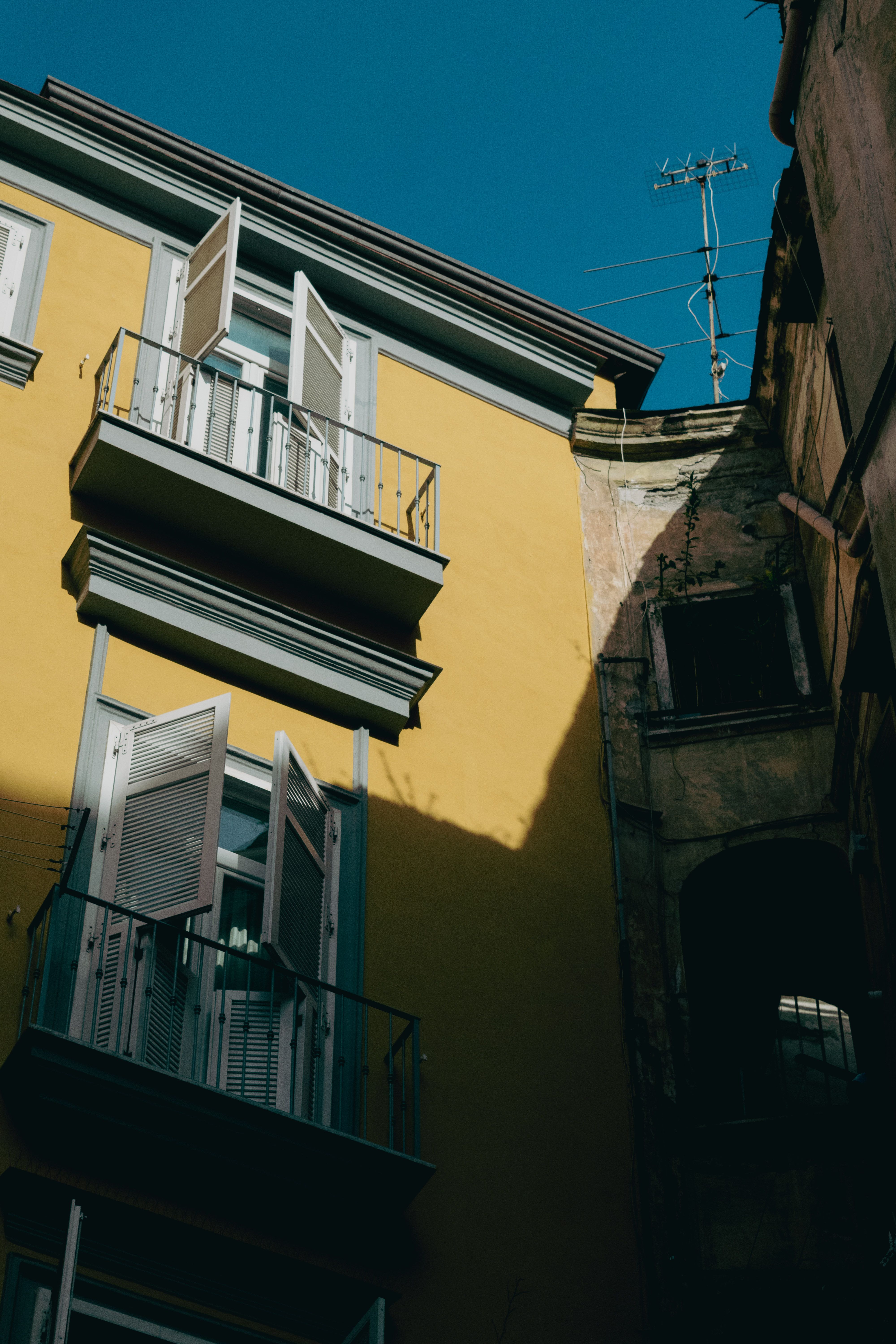 A vibrant yellow building in Naples, Italy, featuring open shutters under a clear blue sky.