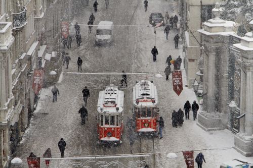 Free A snowy winter scene on Istiklal Avenue featuring iconic red trams and pedestrians. Stock Photo