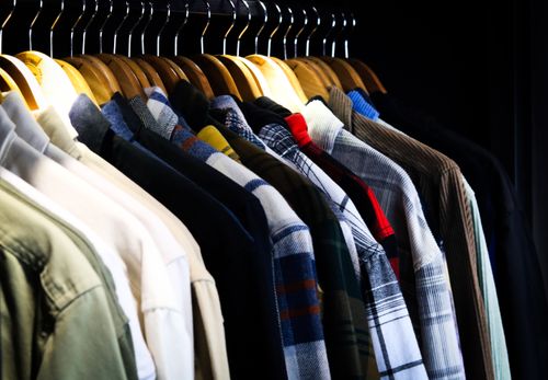 Free Colorful array of men's shirts on hangers in a dimly lit closet, showcasing patterns and textures. Stock Photo