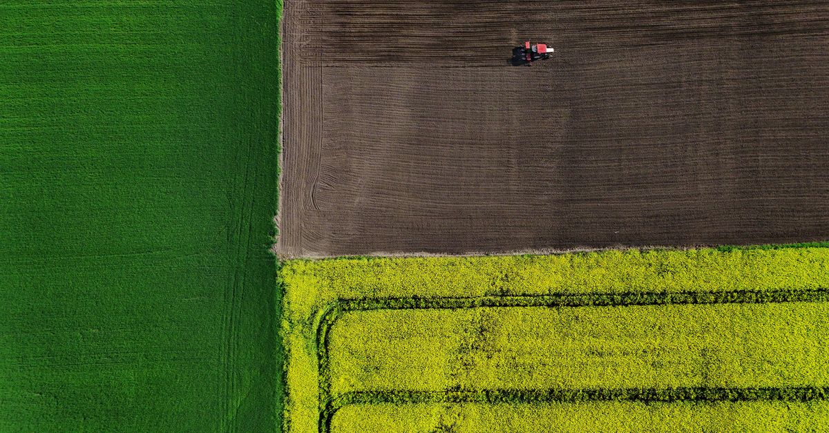 drone flying over a green field with a tractor in the background