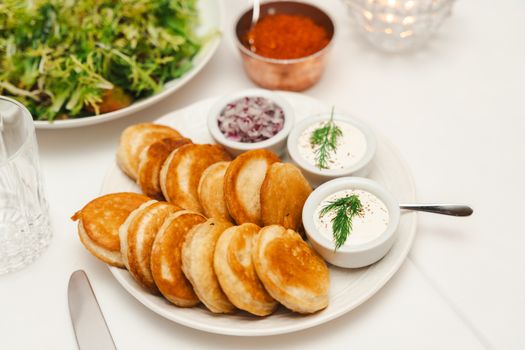 A plate of golden pancakes with sour cream dip and salad, perfect for a savory meal.