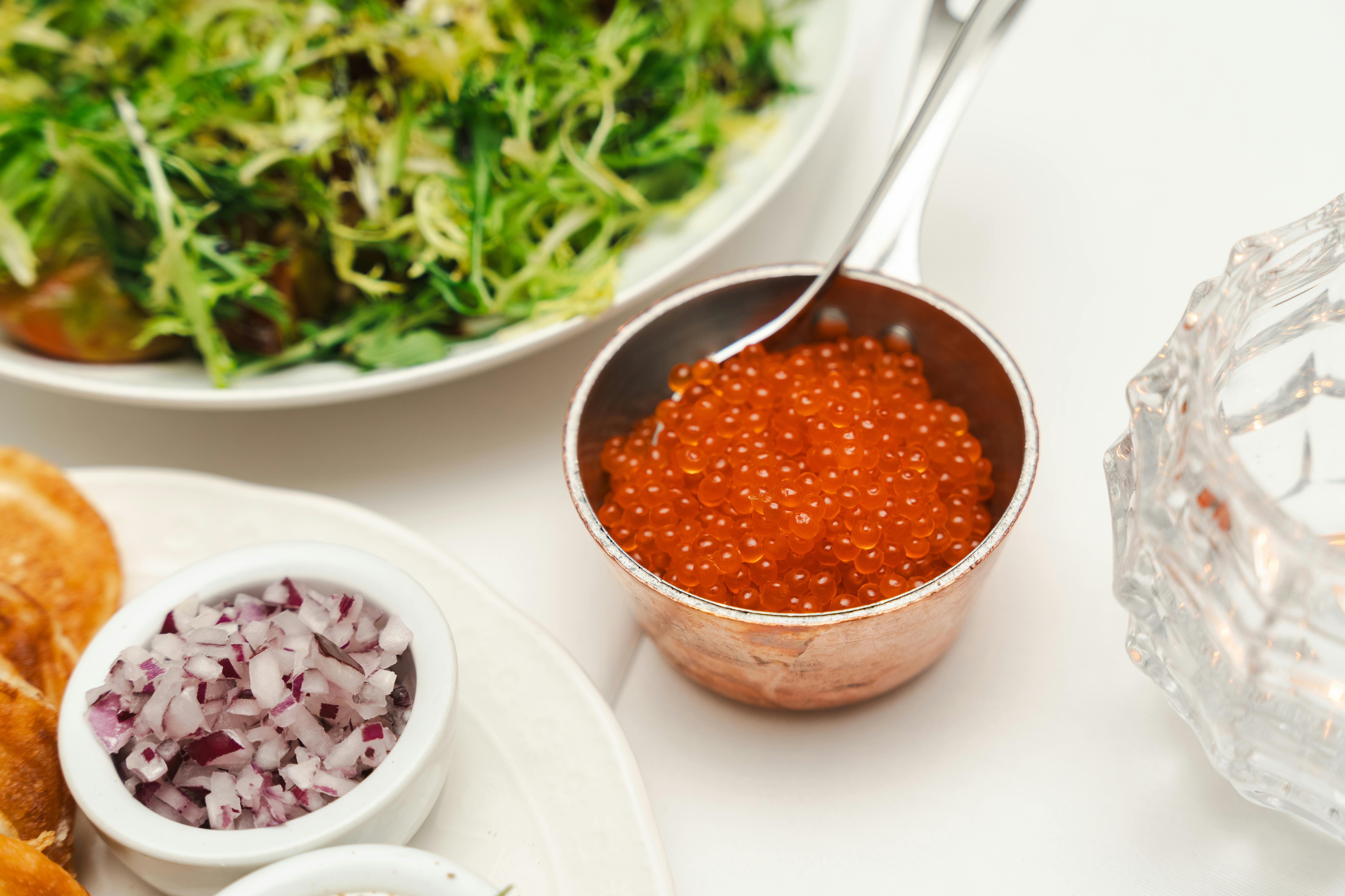 Close-up of gourmet cuisine featuring caviar, fresh salad, and onion in natural light setting.