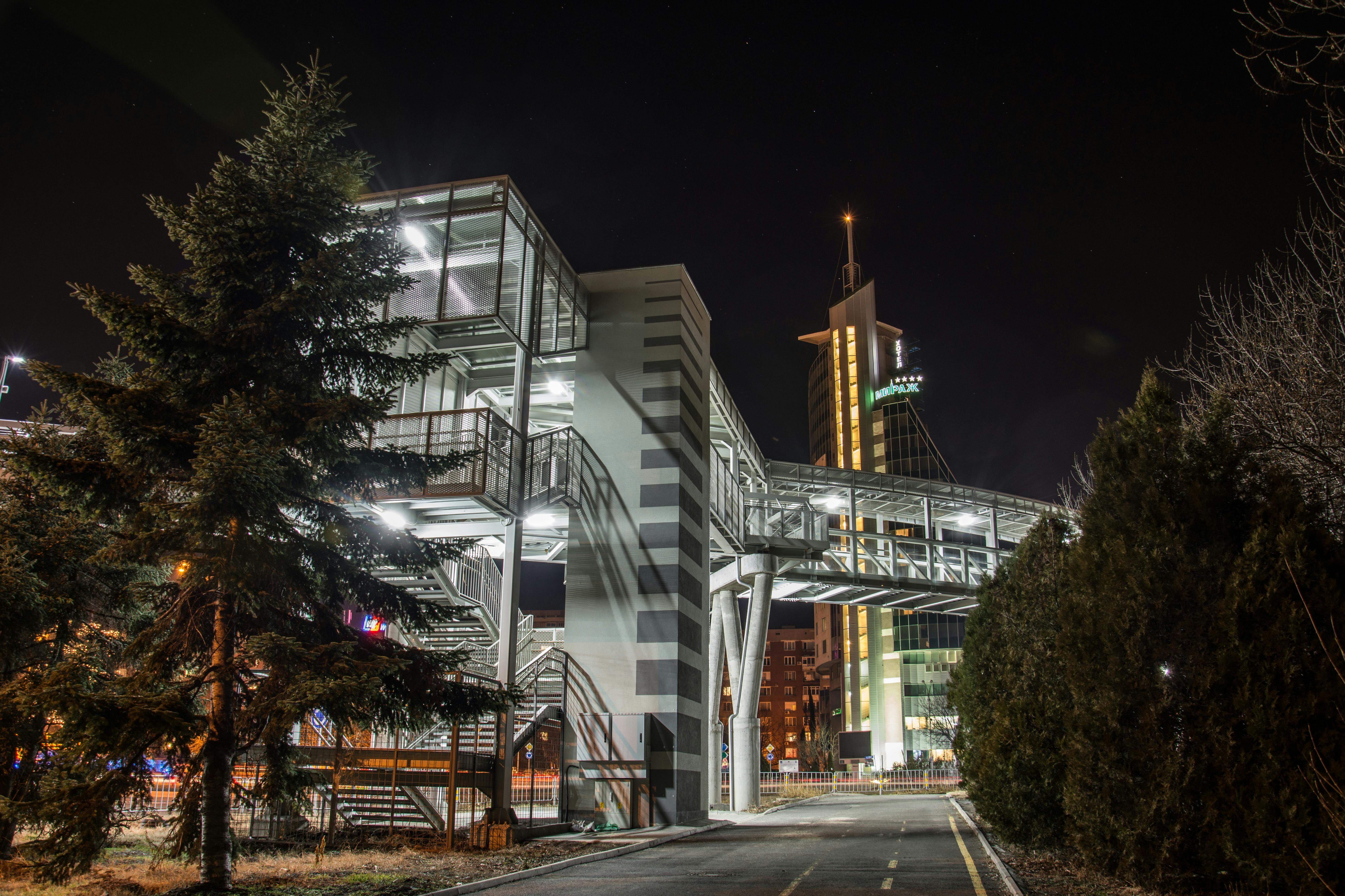 这座照明人行桥位于夜间城市环境中，展现了现代建筑风格