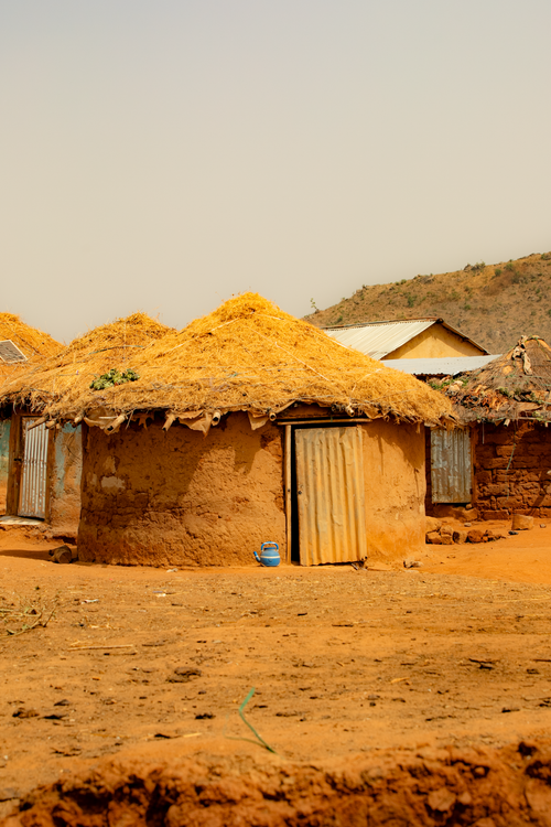 Free Rustic mud huts with straw roofs in a serene rural village landscape. Stock Photo