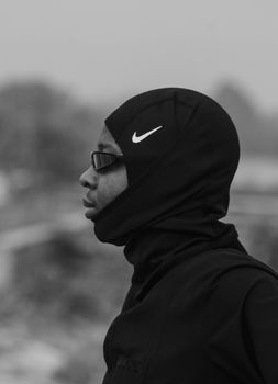 Monochrome side profile of a person wearing a hooded sportswear with sunglasses outdoors.