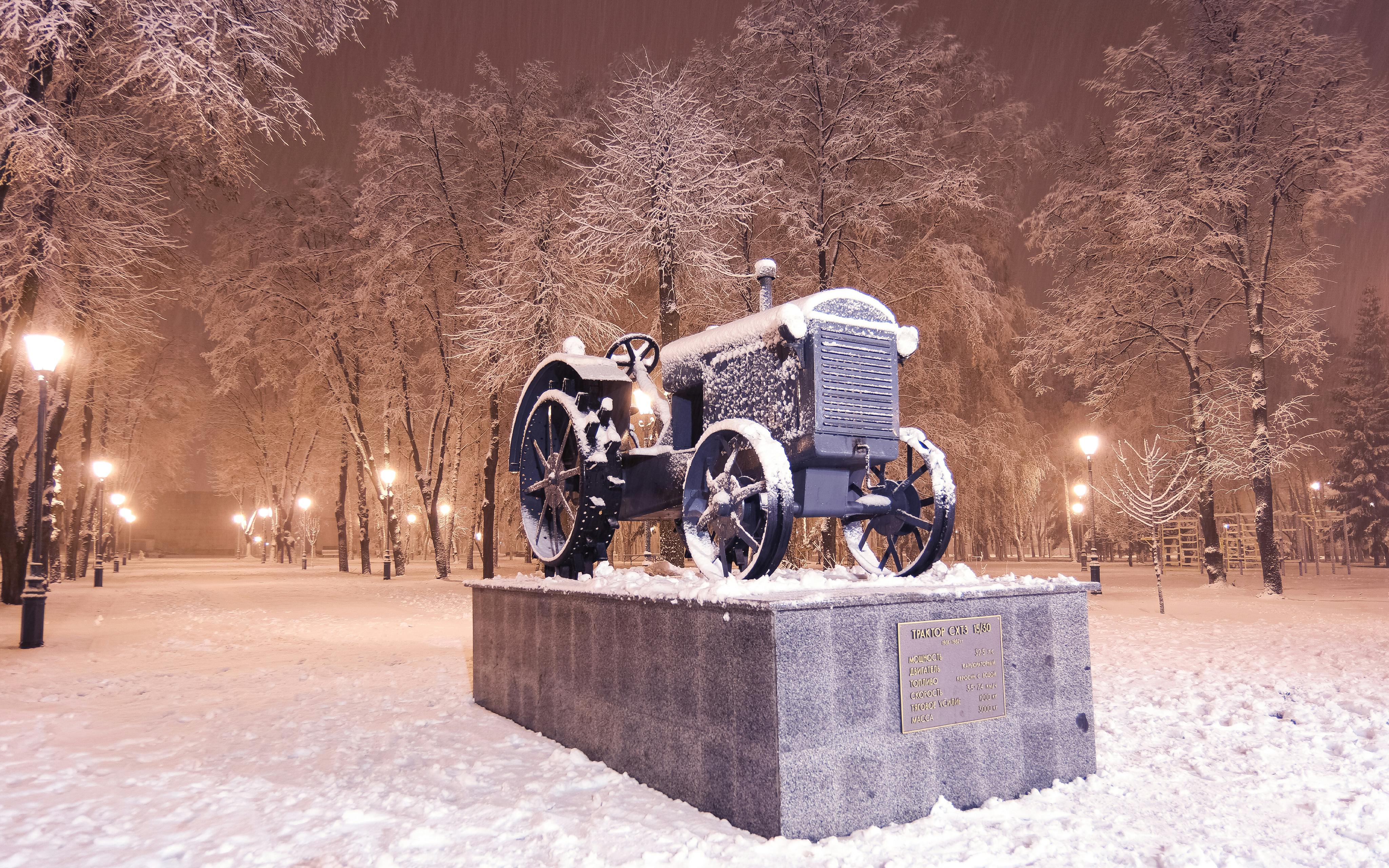 Vintage tractor monument covered in snow on a winter night in Kharkiv Park, Ukraine.