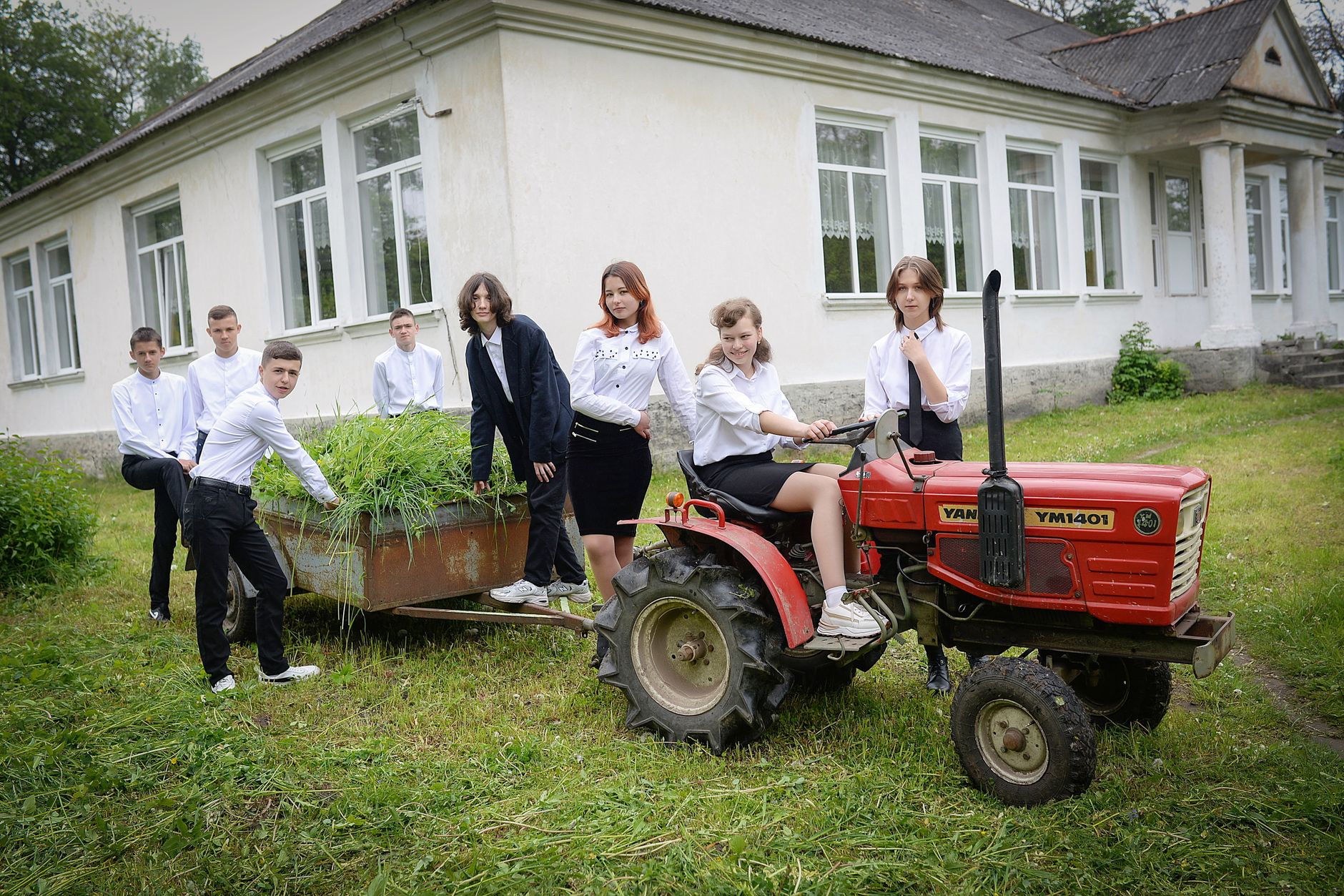 Students posing with a red tractor in a schoolyard, showcasing teamwork and education.