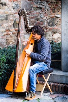A male street musician passionately plays the harp against a rustic brick wall.