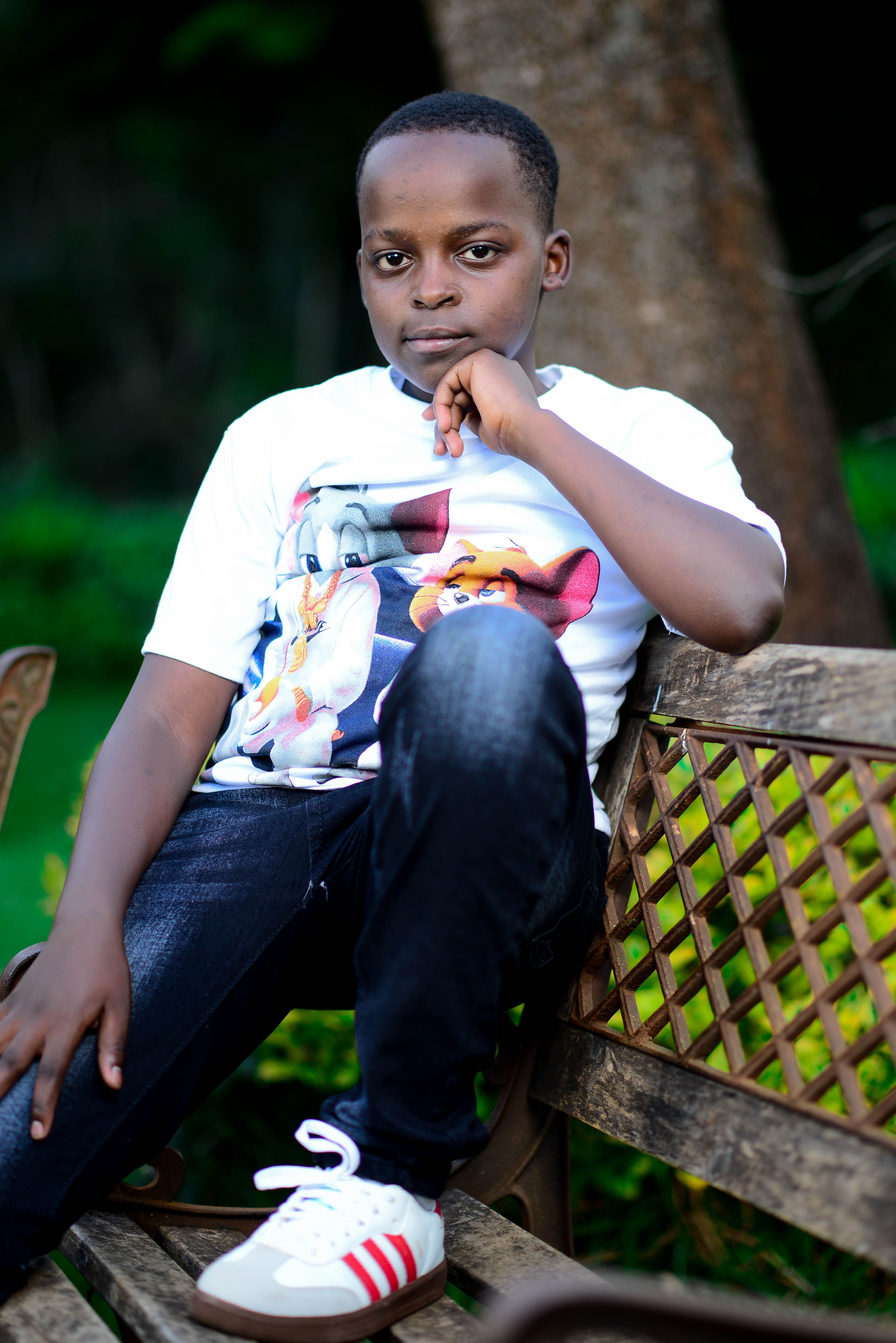 Young boy sitting on a park bench outdoors wearing a cartoon t-shirt.