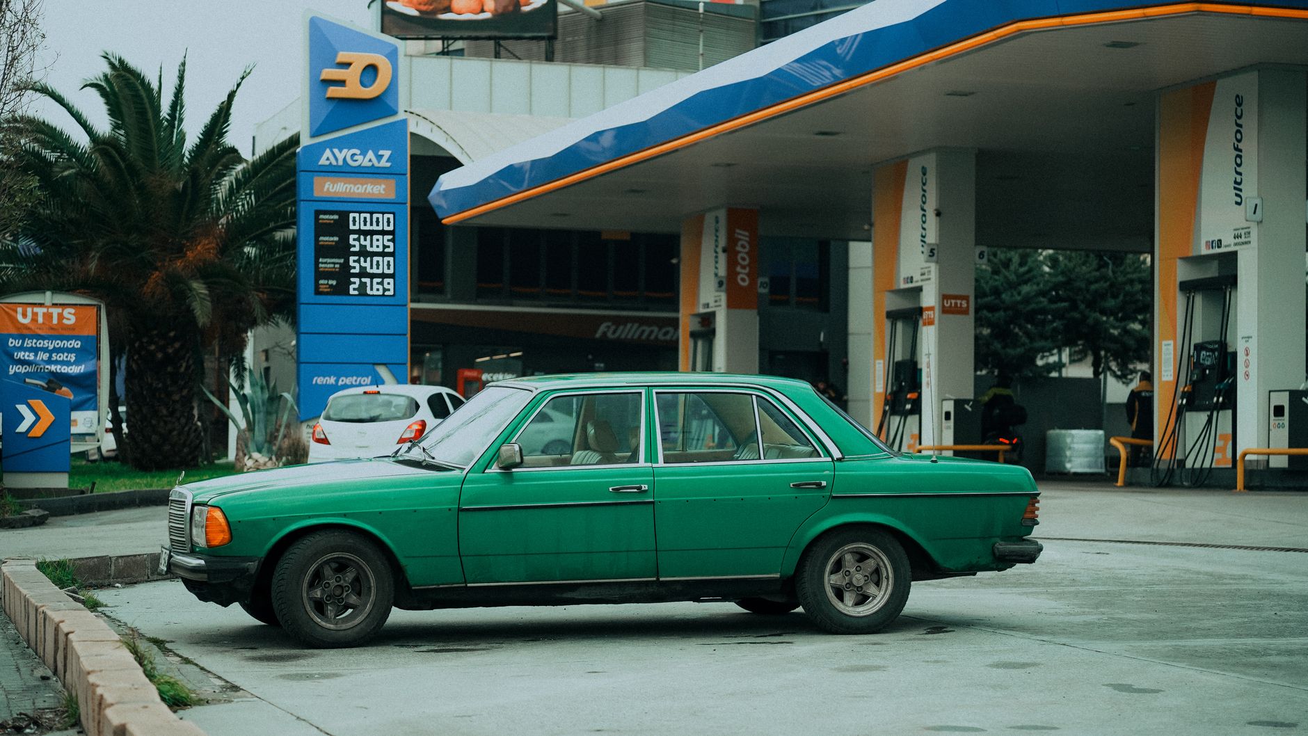 Classic green car parked at a gas station in Istanbul, Türkiye, under overcast weather.