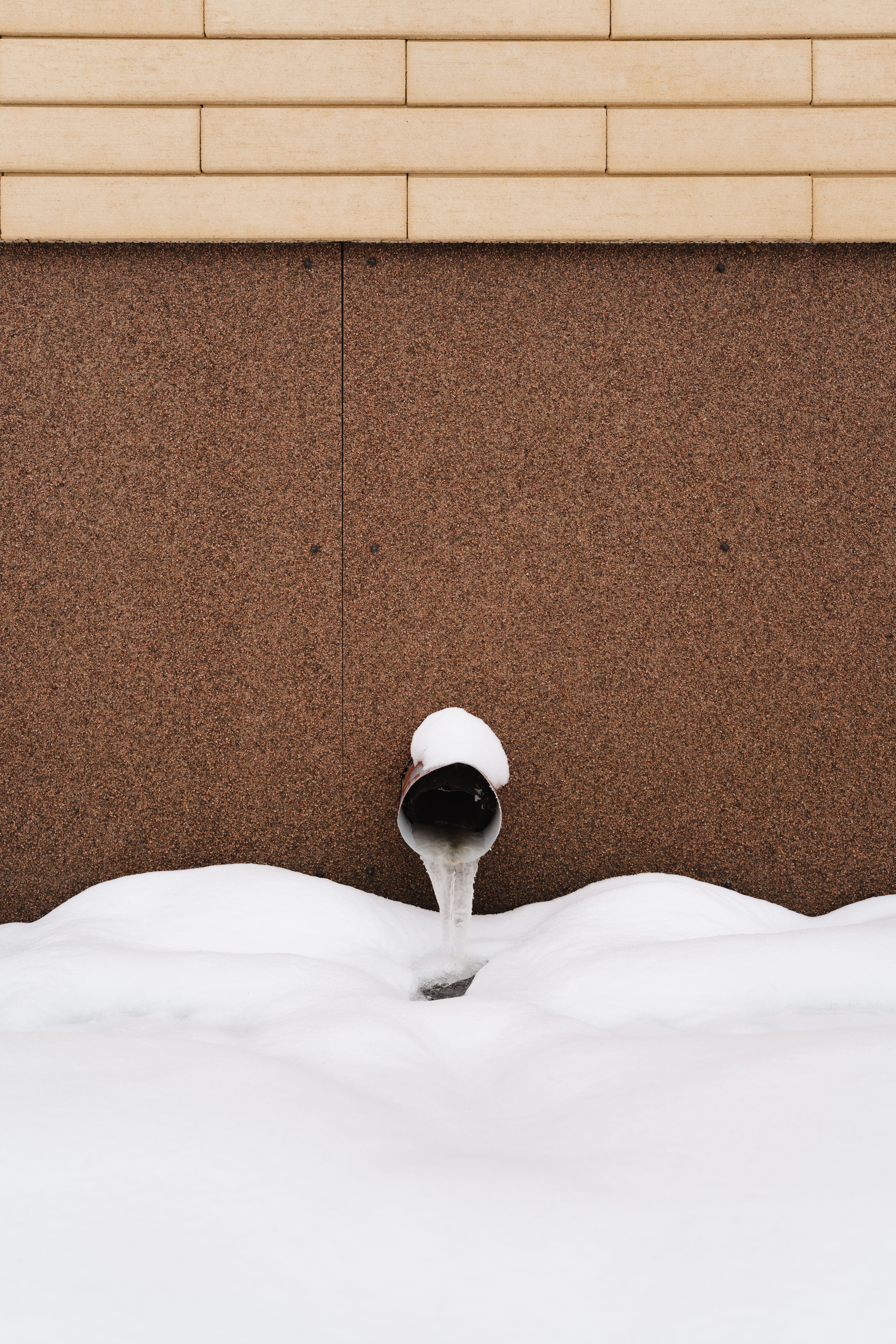 Frozen exterior water pipe beside a snow-covered building wall