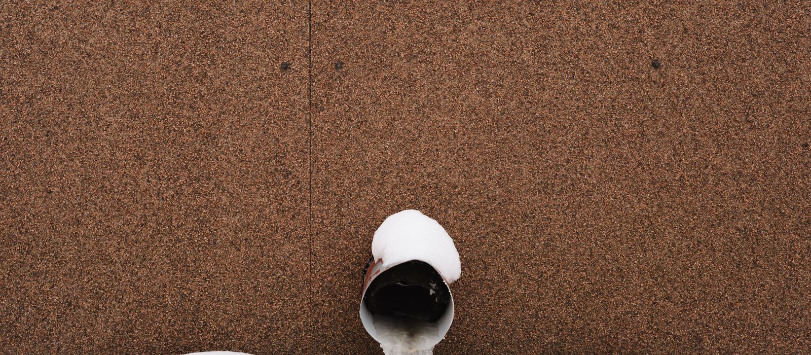 Frozen water pipe against a building wall in snow