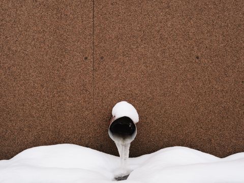 Frozen water pipe against a building wall in snow