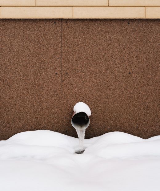 Frozen water pipe against a wall in snow