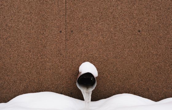 Frozen water pipe against a building wall in snow