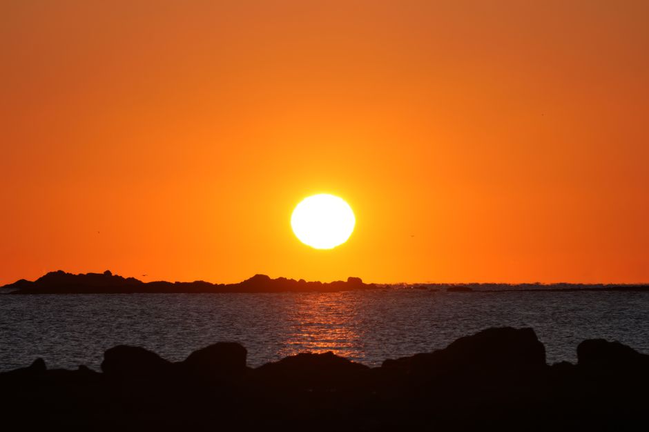 海に沈む鮮やかなオレンジ色の夕日を背景にした岩のシルエット。