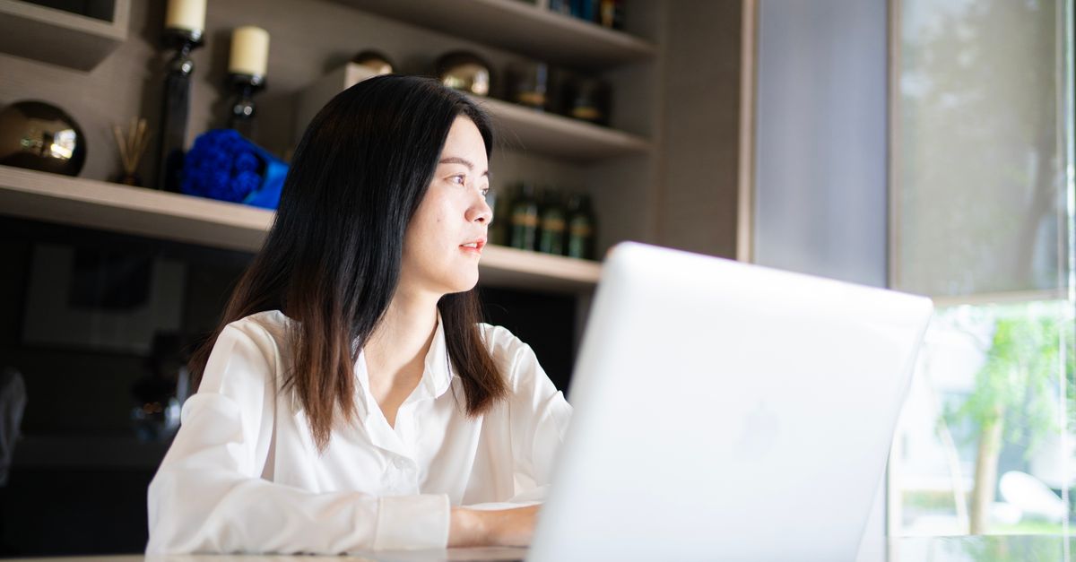 Young Asian businesswoman in a modern home office setting, working on a laptop.