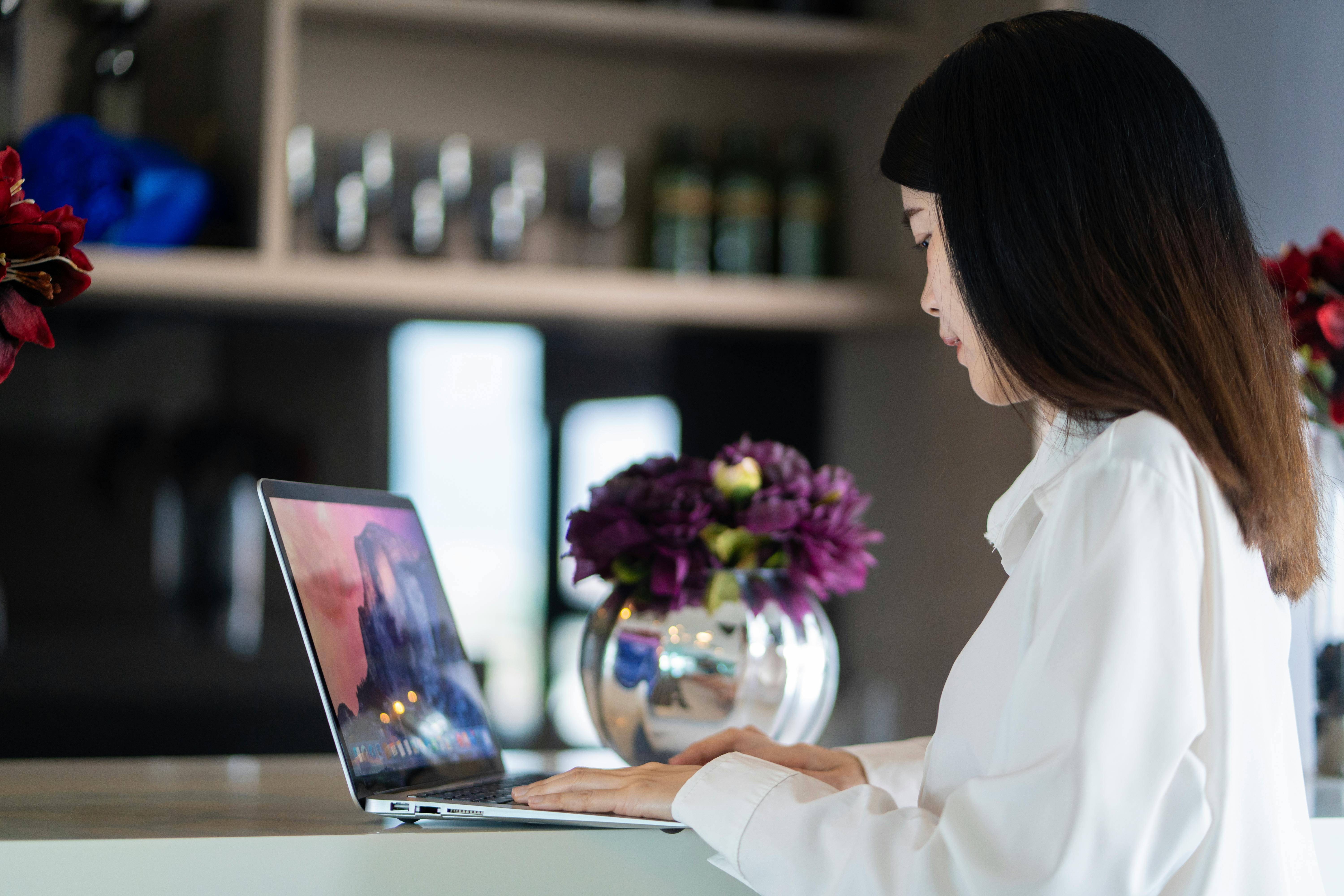 Asian woman working on her laptop in a stylish workspace with floral decor.