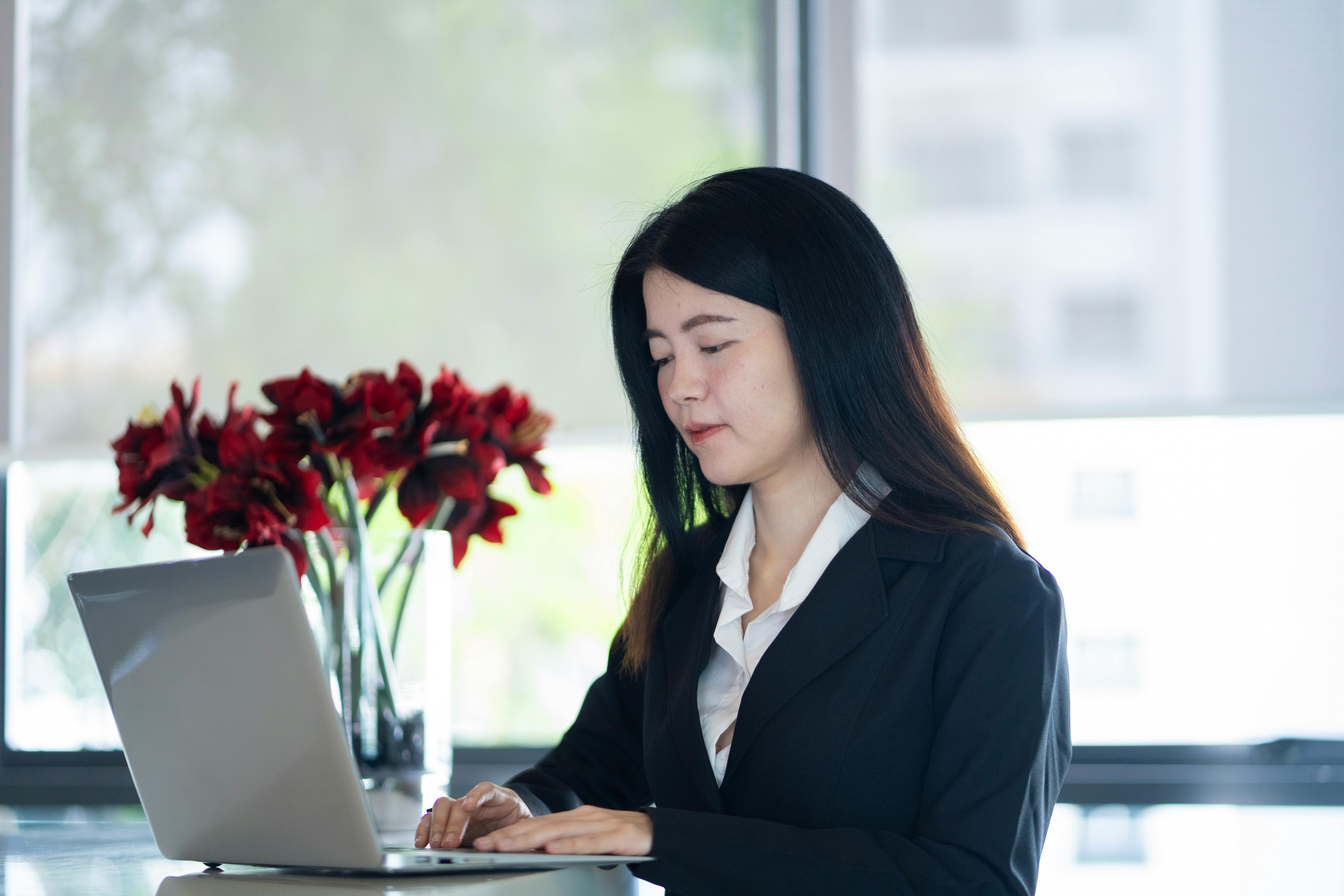 Young Asian businesswoman working on a laptop in a modern office setting.