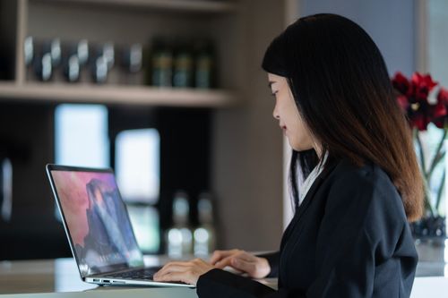 Free Asian woman working on a laptop in a modern home office, blending productivity and style. Stock Photo