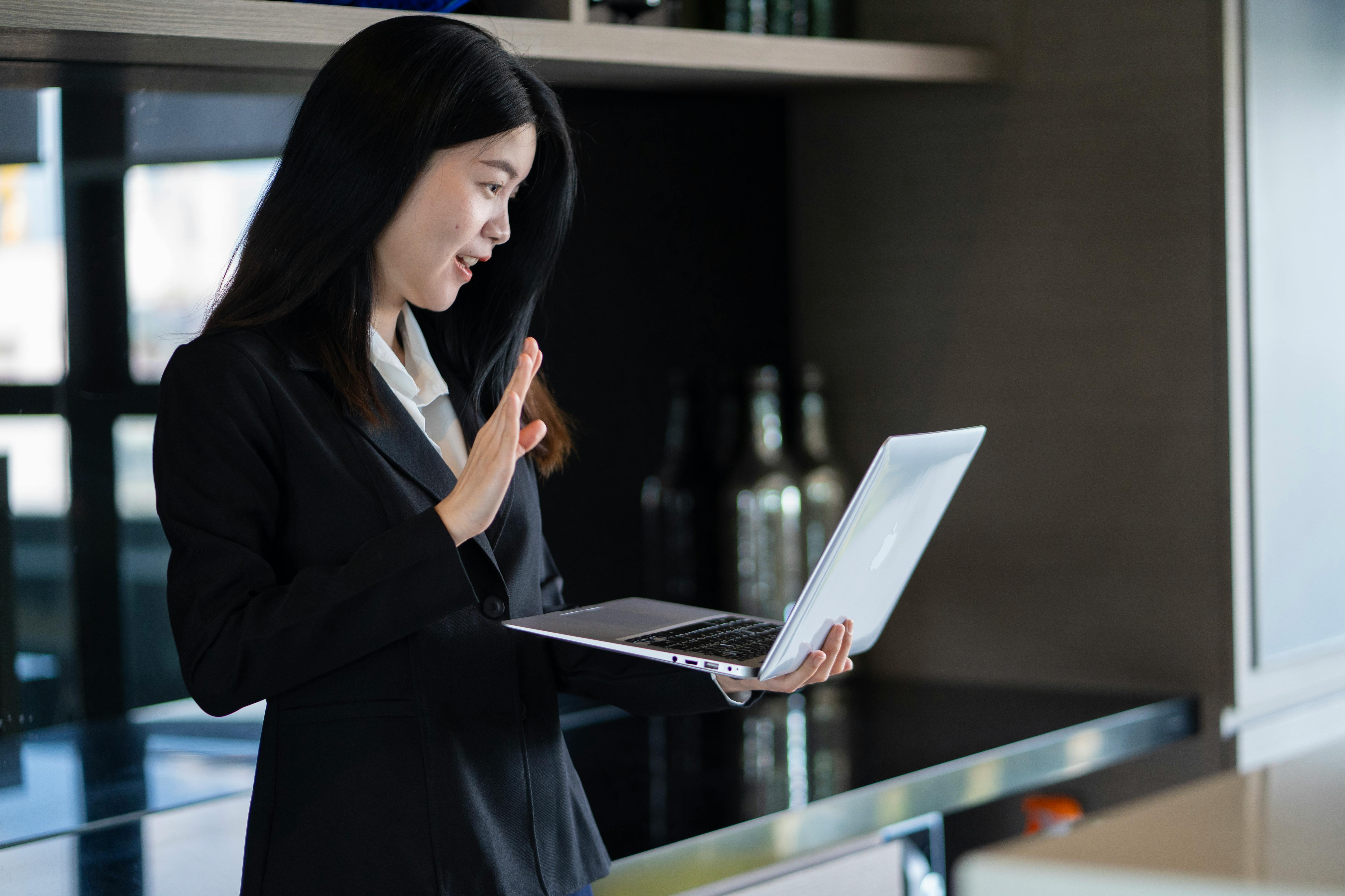 Confident young woman in a black suit engaged in a video call from a home office.