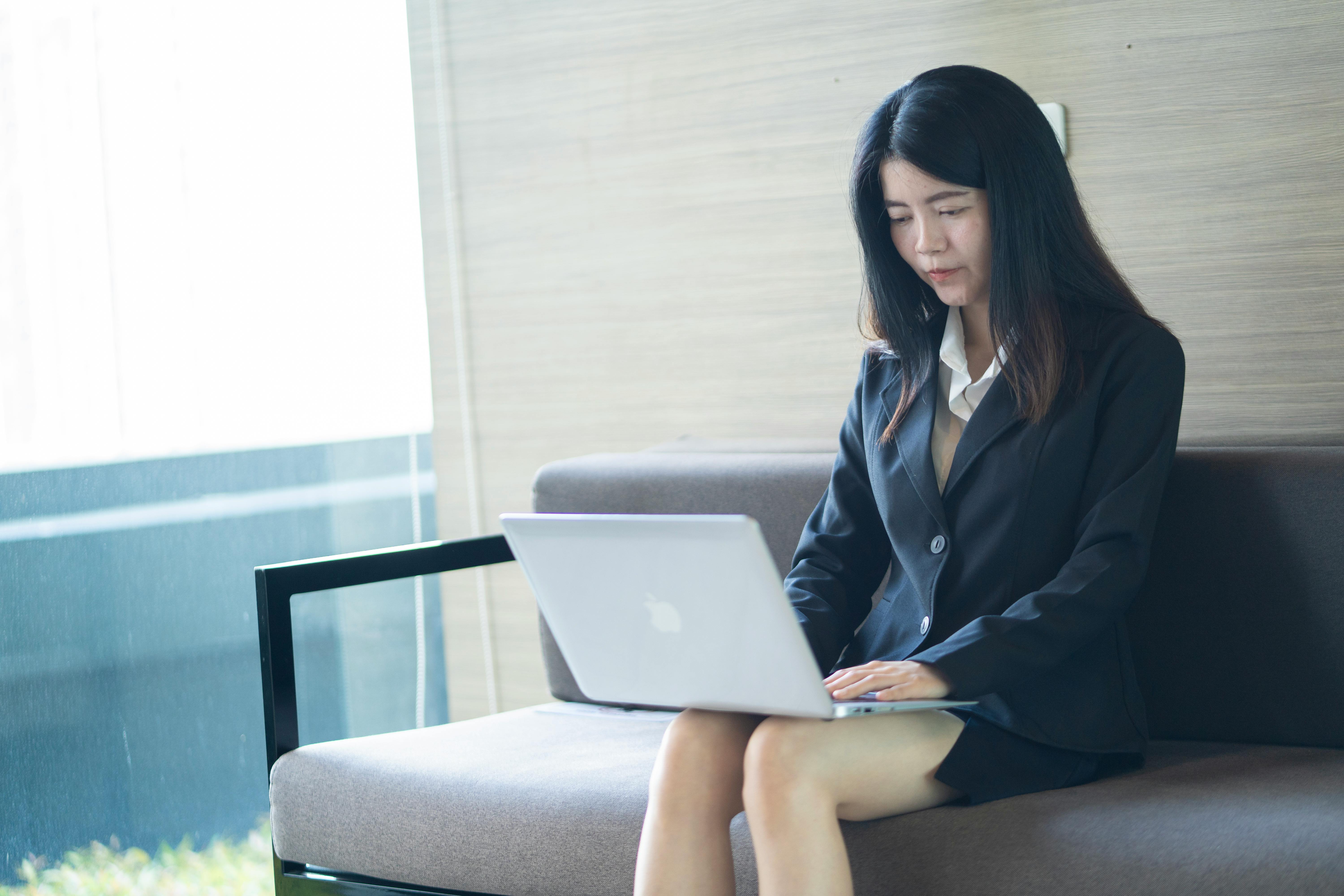 Asian businesswoman in smart casual attire working on laptop in a modern office setting.