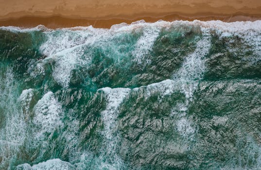 Tranquil aerial view of turquoise waves crashing on the sandy shore of Dolphin Coast, South Africa.