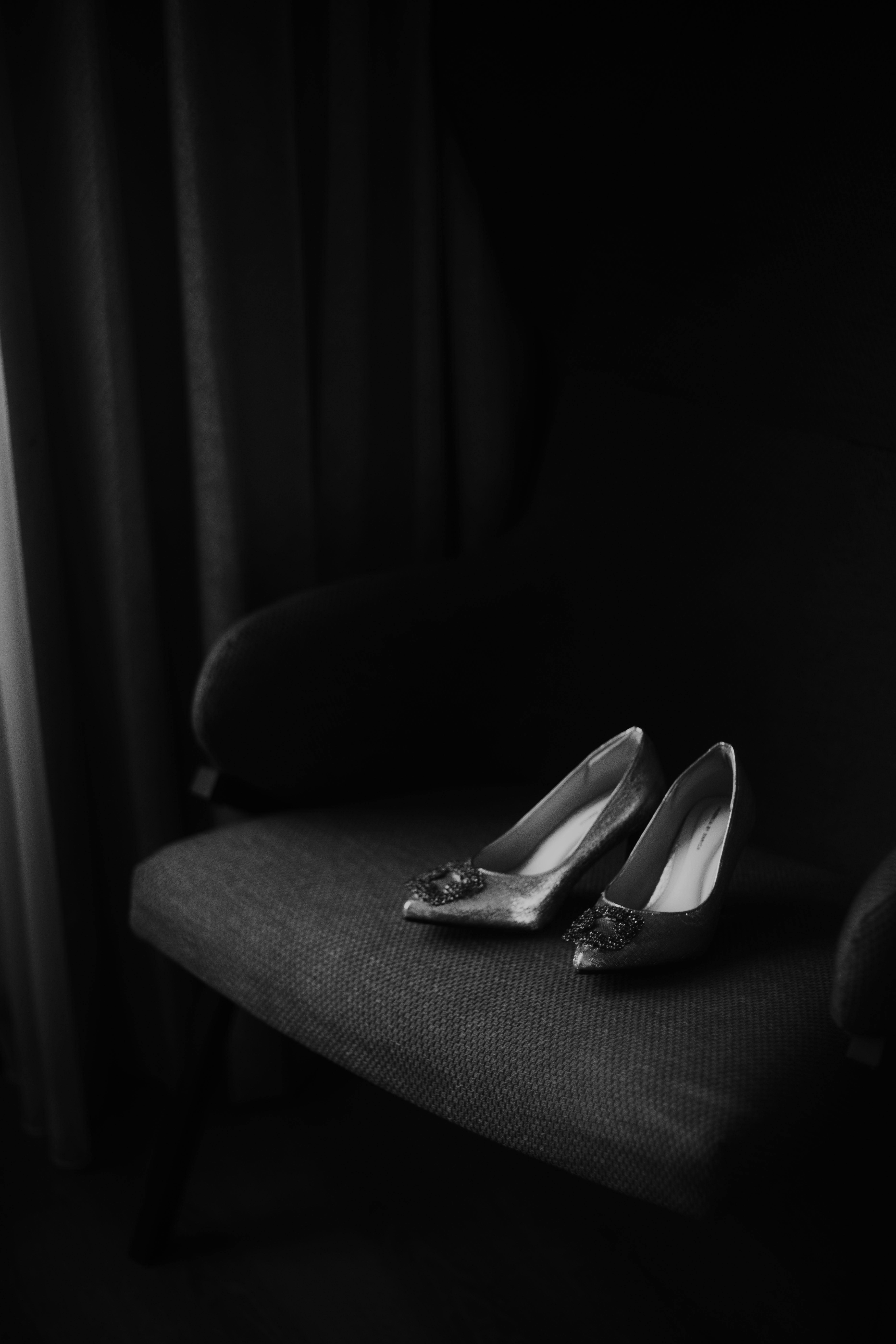 Gratis Foto hitam putih sepatu hak tinggi elegan yang diletakkan di atas kursi gelap dalam pencahayaan redup. Foto Stok