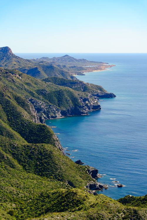 Free Breathtaking aerial view of lush green coastal cliffs by a blue sea under clear skies. Stock Photo