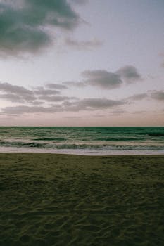 A tranquil winter beach scene at sunset in Ras Al Khaimah, UAE, featuring gentle waves and soft pastel skies.