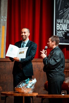 Two presenters at a lively award ceremony with red curtain background.