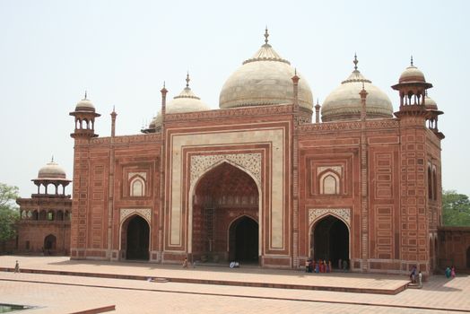 The red sandstone mosque next to the Taj Mahal under a clear sky.
