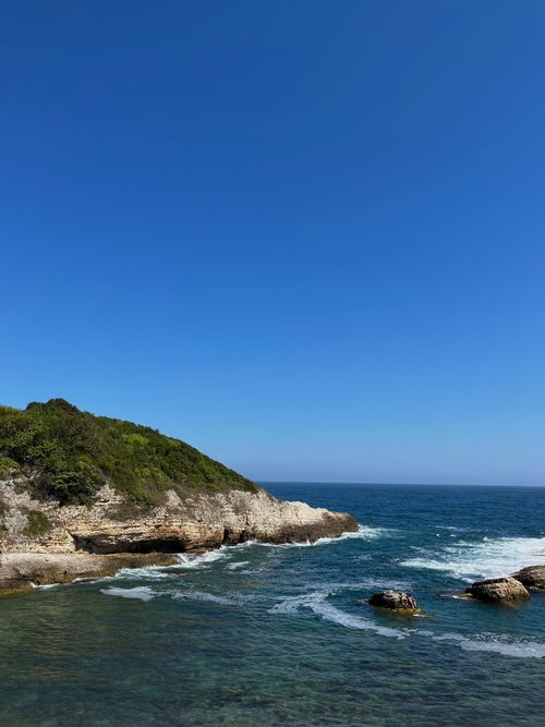 Free Peaceful rocky shoreline under a clear blue sky, with waves lapping at the coast. Stock Photo