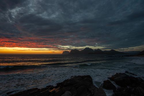 Free Spectacular sunset over rocky seashore and mountains in Nordland, Norway, with vivid clouds and ocean waves. Stock Photo