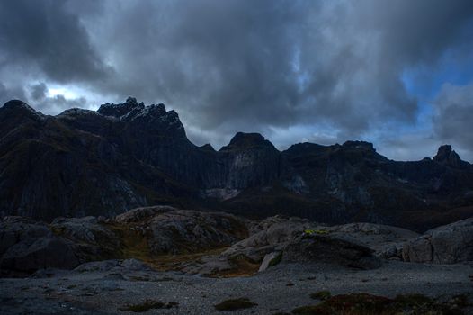Twilight view of dramatic mountain peaks under cloudy sky in Nusfjord, Norway.