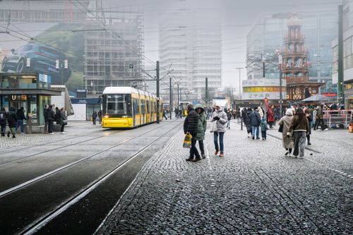 Free Busy city street in Berlin featuring a yellow tram, winter clothing, and bustling pedestrians. Stock Photo