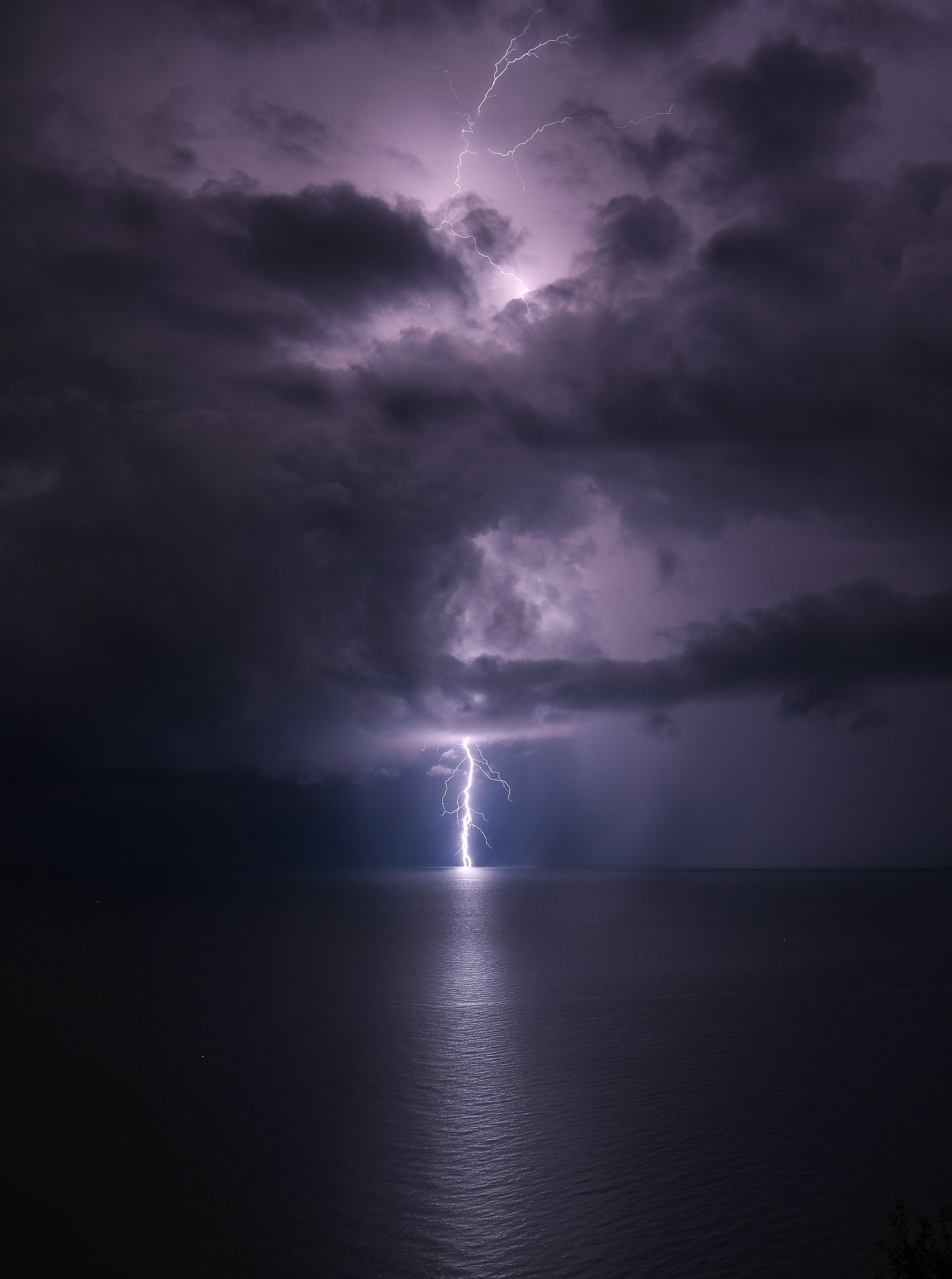 Striking lightning illuminates the night sky over a calm sea, creating a dramatic contrast.