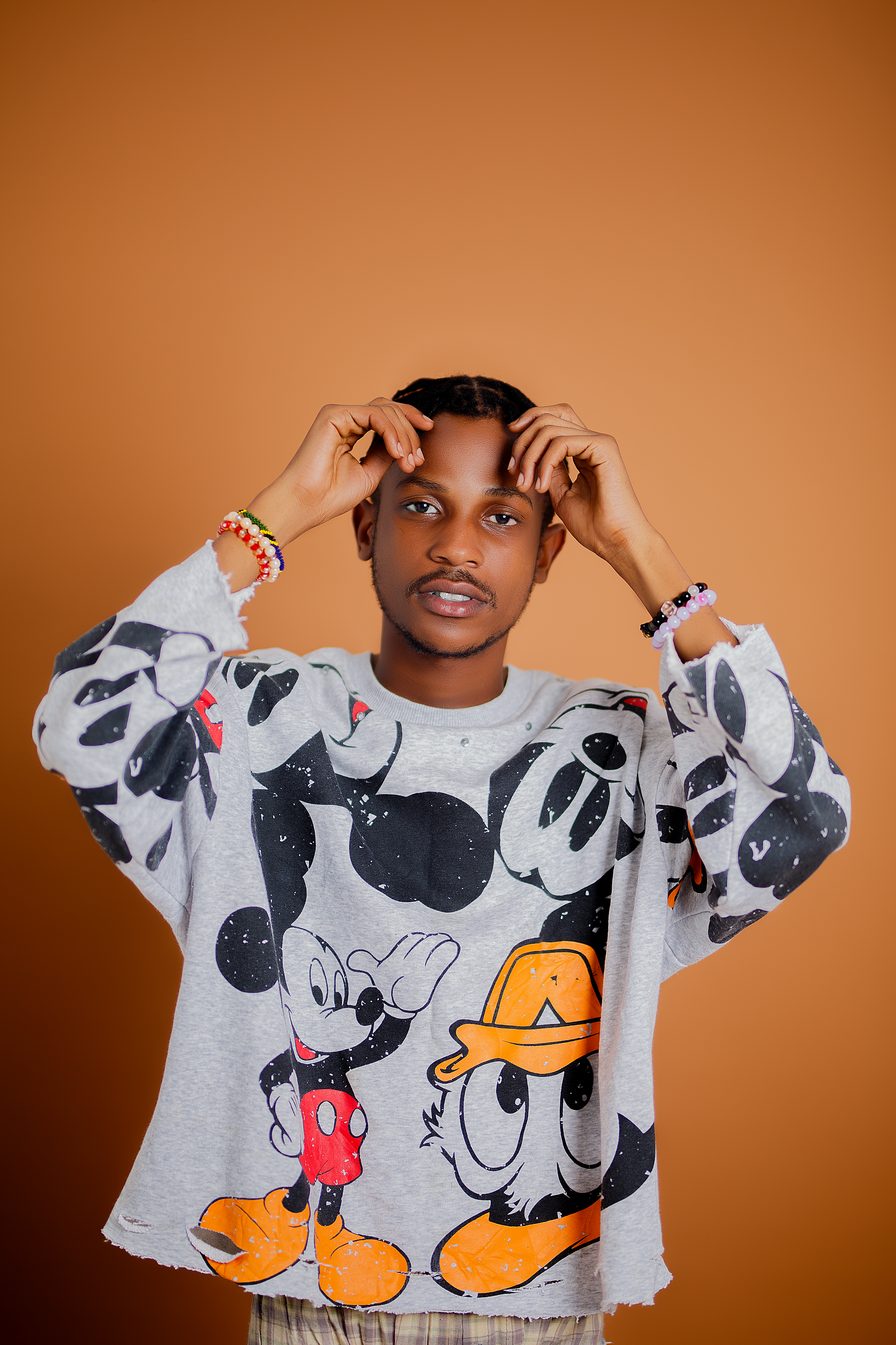Fashionable young adult in animated character sweater posing confidently against orange backdrop.