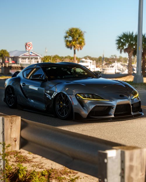 Free A modern sports car parked near a marina with palm trees under a clear sky. Stock Photo