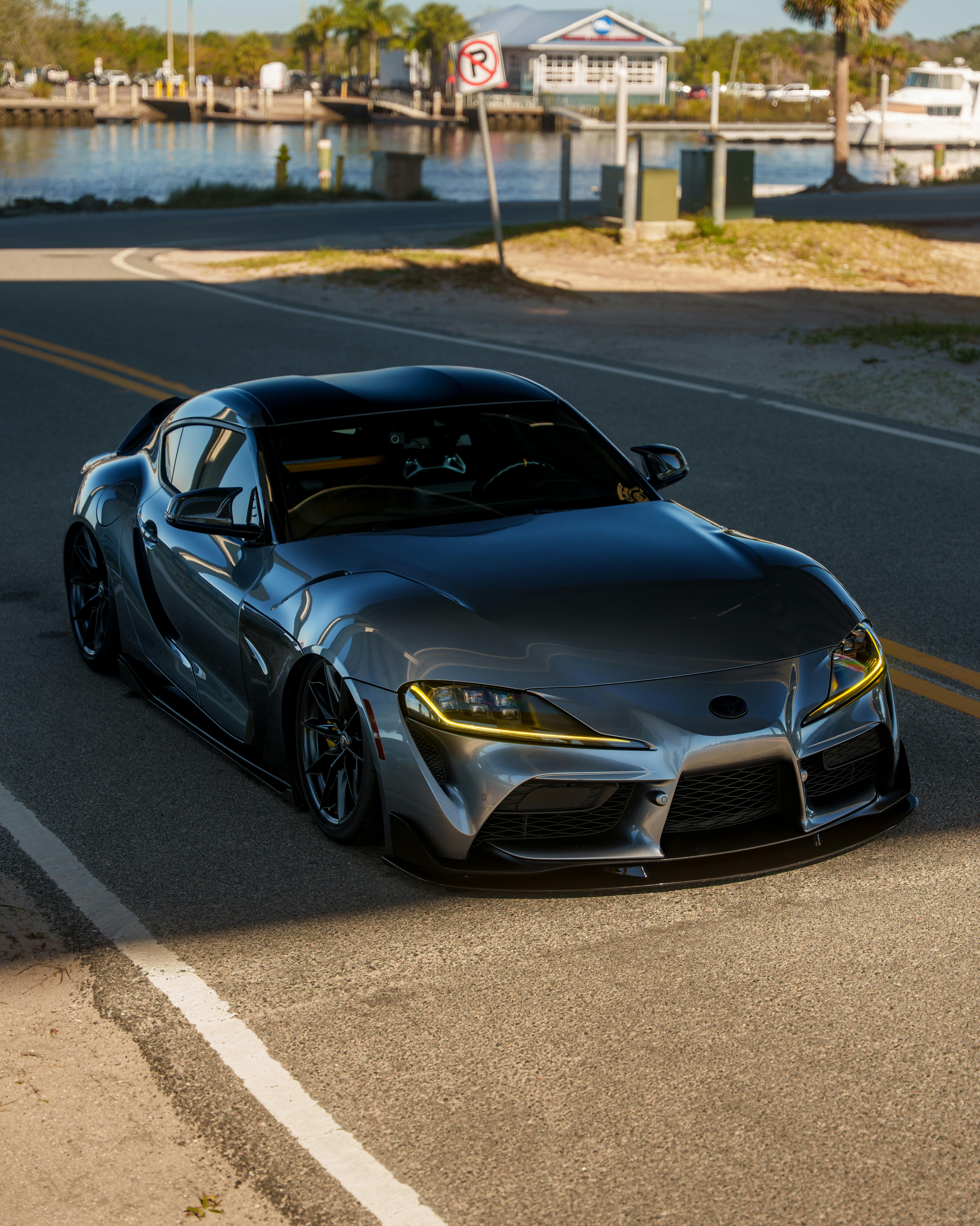 A stylish silver sports car parked on a coastal road with a marina backdrop.