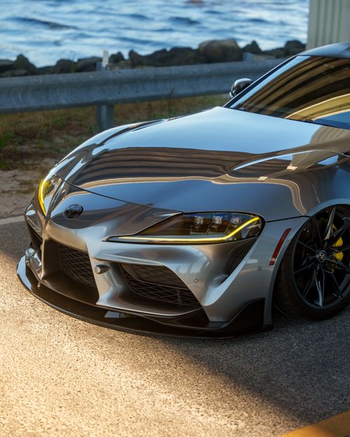 Free A shiny silver sports car parked by an ocean road under bright daylight. Stock Photo