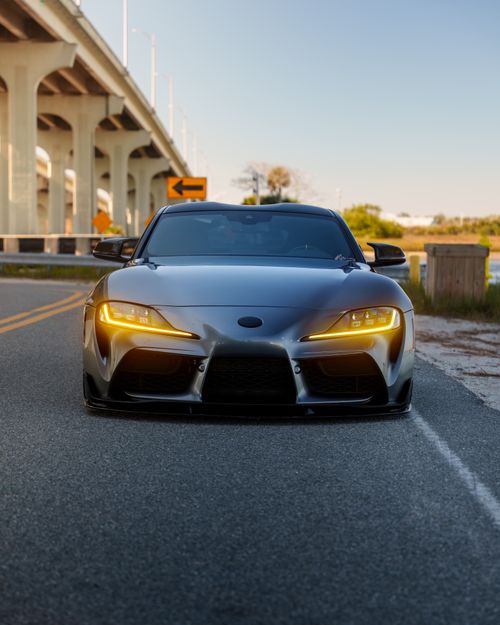 Free A modern sports car with headlights on, parked on an empty road under a bridge at dusk. Stock Photo