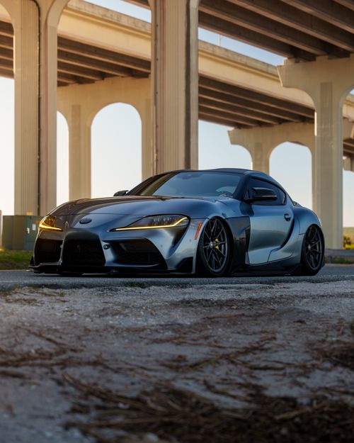 Free Sleek silver sports car parked under an urban bridge at sunset, showcasing elegance and power. Stock Photo