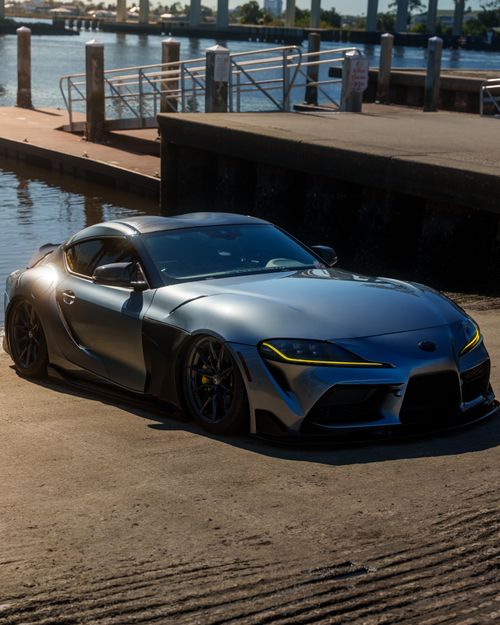 Free A modern silver sports car highlighted by the warm glow of sunset by a peaceful waterfront. Stock Photo